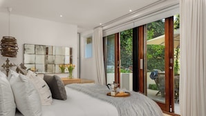 Un dormitorio moderno con una cama grande, una mesita de centro y vistas al jardín a través de un ventanal corredero.
