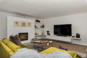 Una sala de estar moderna con sofá, mesa de centro, chimenea, televisor y elementos decorativos.