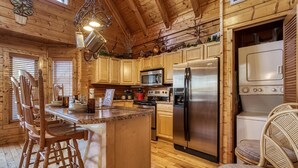 A wooden cabin kitchen with a central island, wooden chairs, a refrigerator, microwave, stove, and a sink.
