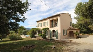 A two-story house with a balcony, a stone archway, and a gravel driveway.
