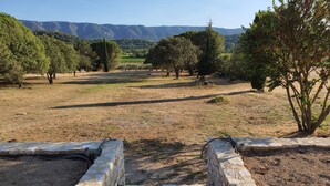 A stone well in a dry, grassy field with trees and mountains in the background.