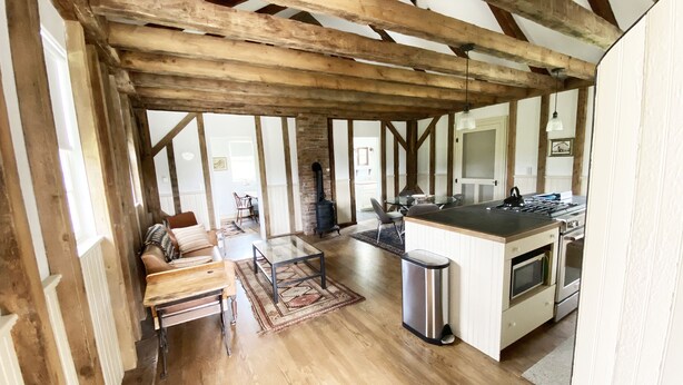 A spacious open-plan living area with a wooden ceiling, a dining table, and a kitchen with a stove and sink.