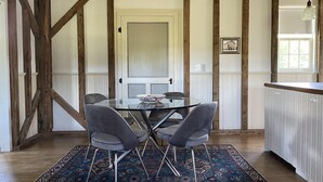 A dining area with a glass table and four chairs, a patterned rug, wooden beams, and a white door.