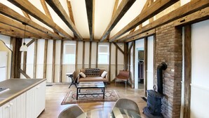 A spacious loft with exposed wooden beams, a cozy sofa set, a glass coffee table, and a brick fireplace.