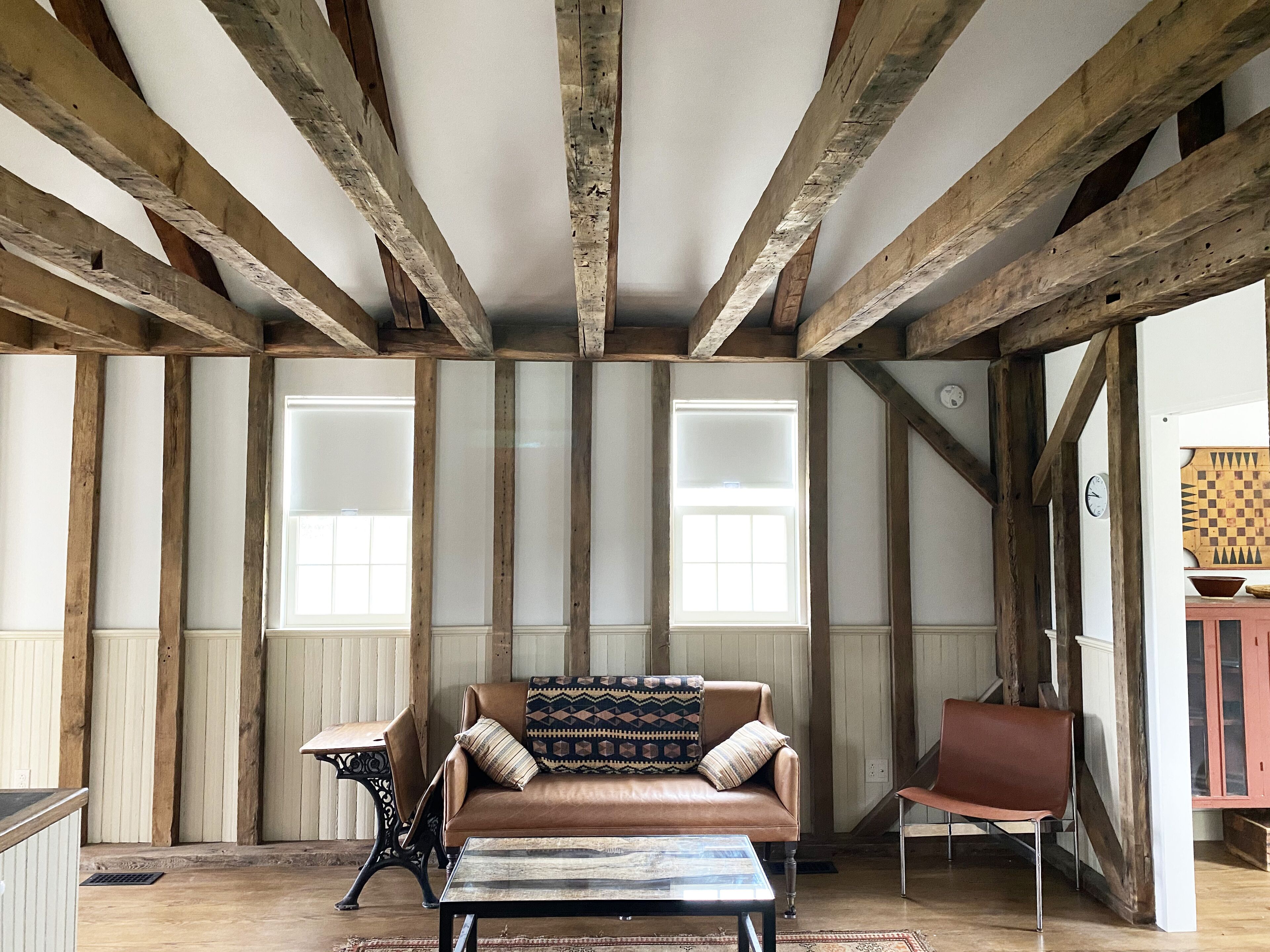Ein Zimmer mit freiliegenden Holzbalken, einem Ledersofa, einem Tisch und einem Stuhl.