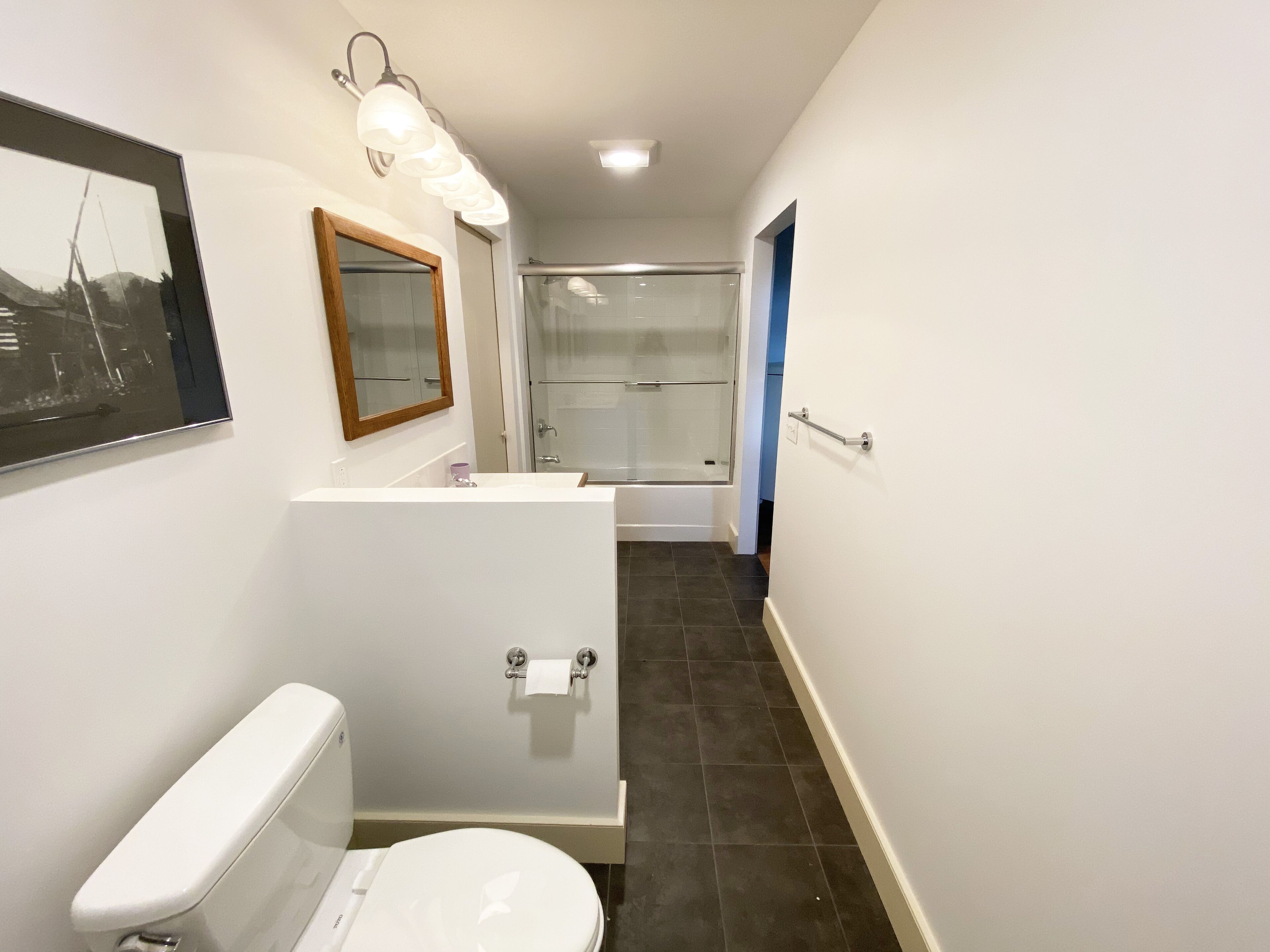 A bathroom with a toilet, sink, mirror, and shower.