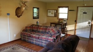 A living room with a plaid sofa, a mounted deer head, a wooden floor, and a door with a sign.