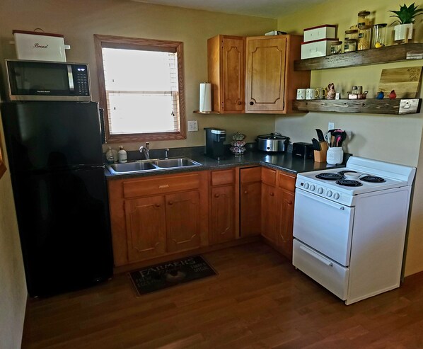 A kitchen with wooden cabinets, a black refrigerator, a white stove, and a window with blinds.