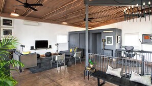 A spacious living area with a large TV, seating, and a balcony with a railing. - Spacious & unique railyard loft w/panoramic balcony views (Santa Fe)
