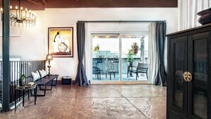 A spacious room with a bench, a table with a lamp, a large painting, and a sliding glass door leading to an outdoor area. - Spacious & unique railyard loft w/panoramic balcony views (Santa Fe)