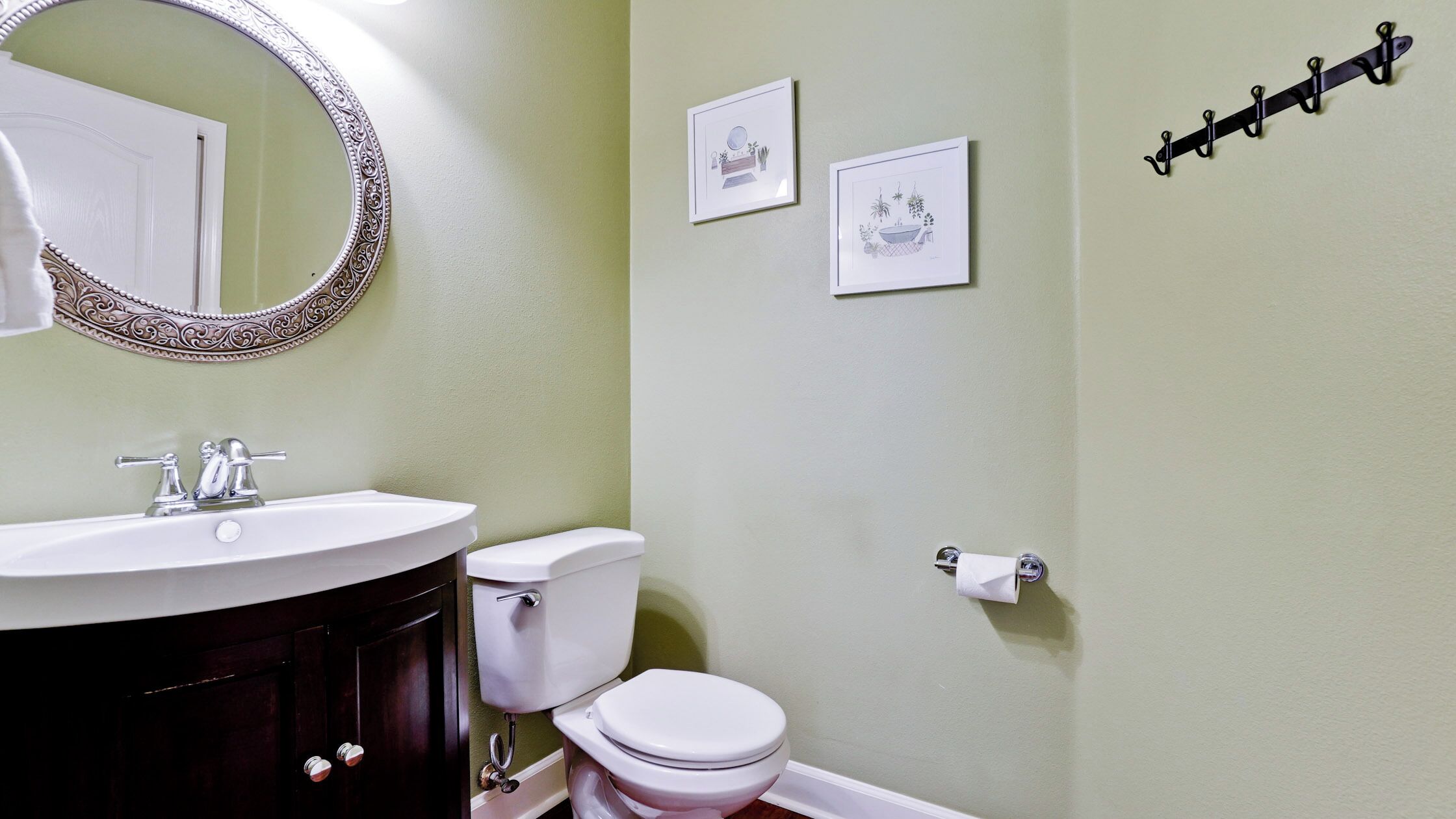 Un baño con un lavamanos blanco, un inodoro y un espejo con un marco decorativo. Hay dos cuadros enmarcados en la pared.