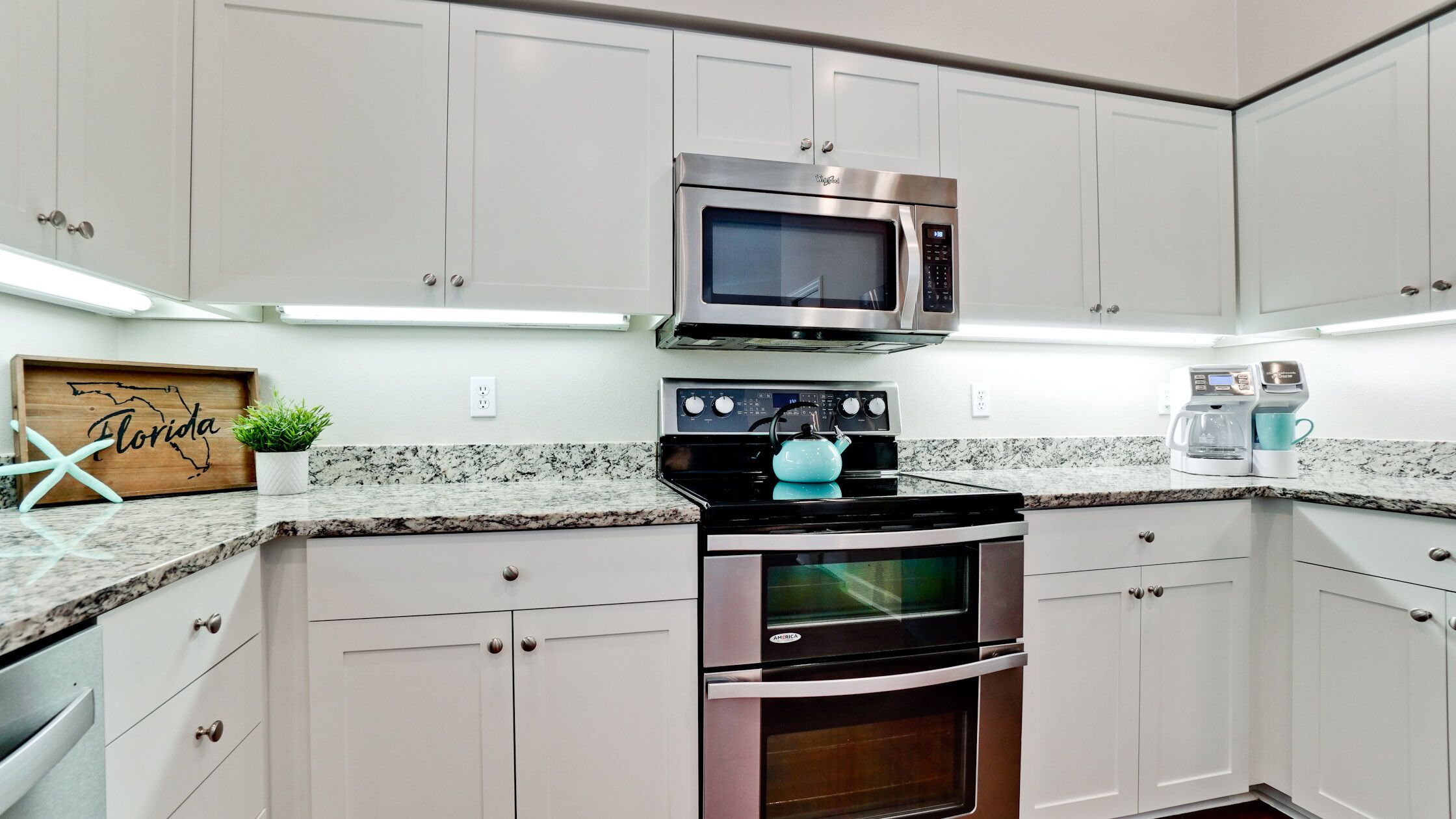 A kitchen with white cabinets, a microwave, a stove, and a coffee maker.