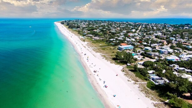 Eine Luftaufnahme einer Küstenstadt mit einem langen Sandstrand, klarem türkisblauem Wasser und einer dichten Bebauung entlang der Küste.