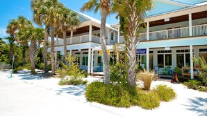 Ein Strandhotel mit mehreren Balkonen, Palmen und einem Schild für 'Olive Oil Orchard'.
