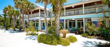A beachfront hotel with multiple balconies, palm trees, and a sign for 'Olive Oil Orchard'.
