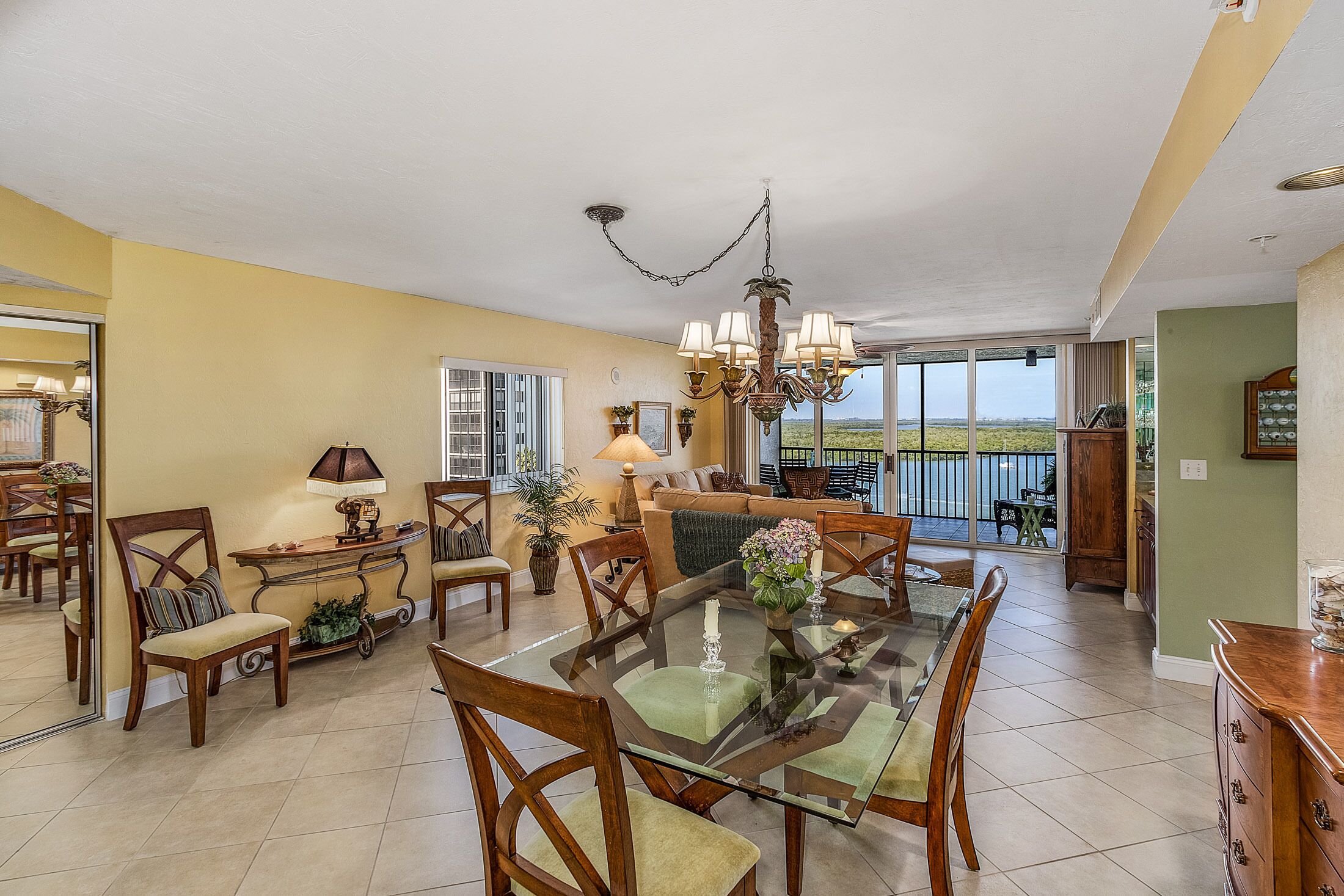 A spacious dining area with a glass table, wooden chairs, and a chandelier.