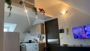 Une cuisine moderne dotée d’appareils électroménagers intégrés, un coin repas avec un téléviseur et un escalier agrémenté de plantes.