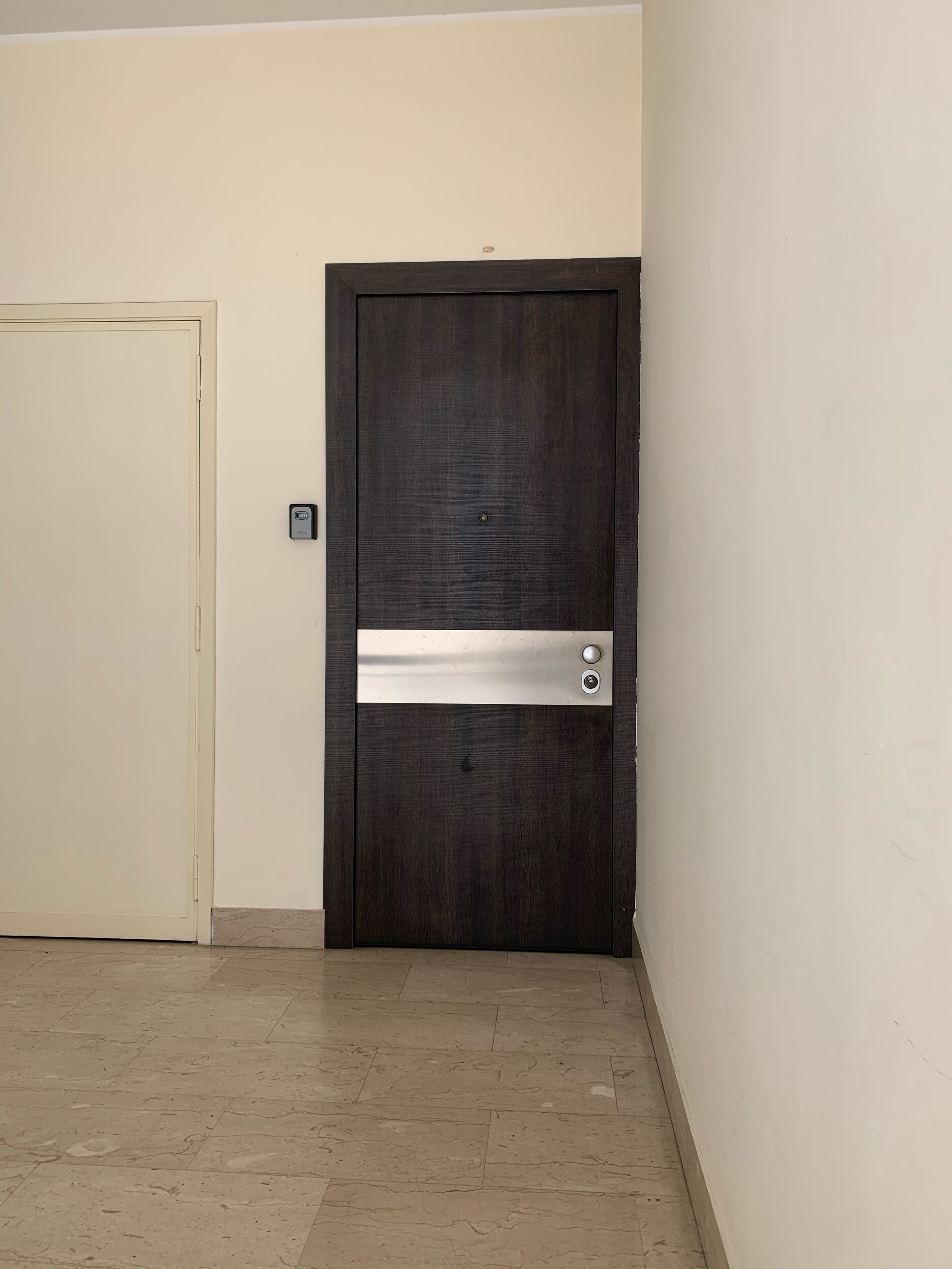 Eine geschlossene Tür mit einem Metallgriff und Schlüsselloch, eine schlichte Wand und ein gefliester Boden.