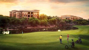 Un parcours de golf avec un étang, des arbres et des bâtiments en arrière-plan.