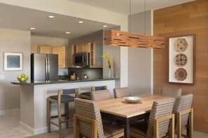 A modern kitchen with wooden cabinets, stainless steel appliances, and a dining area with wicker chairs.
