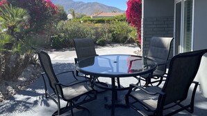 Una mesa de vidrio redonda con cuatro sillas, rodeada por un jardín con flores rojas y vistas a la montaña.
