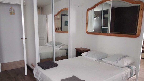 A bedroom with a bed, a nightstand, a mirror, and a door. - Large F3 apartment with balcony (Pierrelaye)