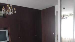 A bedroom with a bed, a television on a stand, dark wooden wardrobes, and a chandelier. - Large F3 apartment with balcony (Pierrelaye)