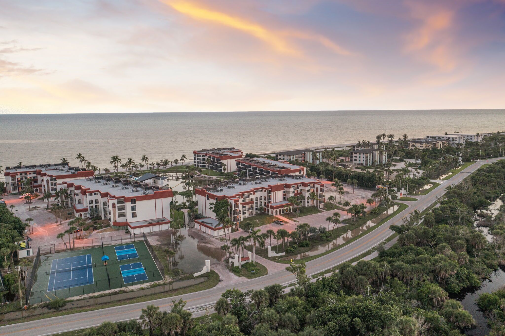 A resort with multiple buildings, a tennis court, and a view of the ocean.
