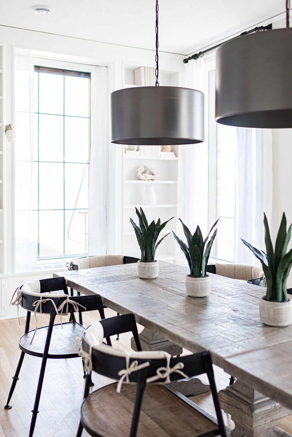 A modern dining area with a wooden table, black chairs, and potted plants.