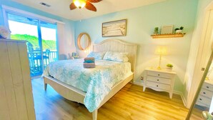 Une chambre à coucher comprenant un lit, une table de chevet, un ventilateur de plafond, une fenêtre et une vue sur l’extérieur.