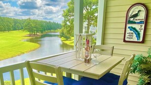 Une terrasse en bois avec une table et des chaises, offrant une vue sur une rivière et un paysage verdoyant.