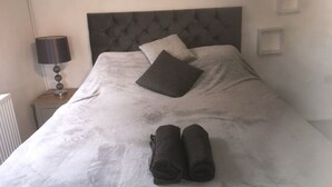 A neatly made bed with a tufted headboard, two pillows, and rolled towels on a white bedspread. - One Bedroom Maisonette with Terrace, Kidderminster (Kidderminster)