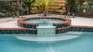 Una piscina con un jacuzzi, rodeada de una terraza con baldosas y plantas.