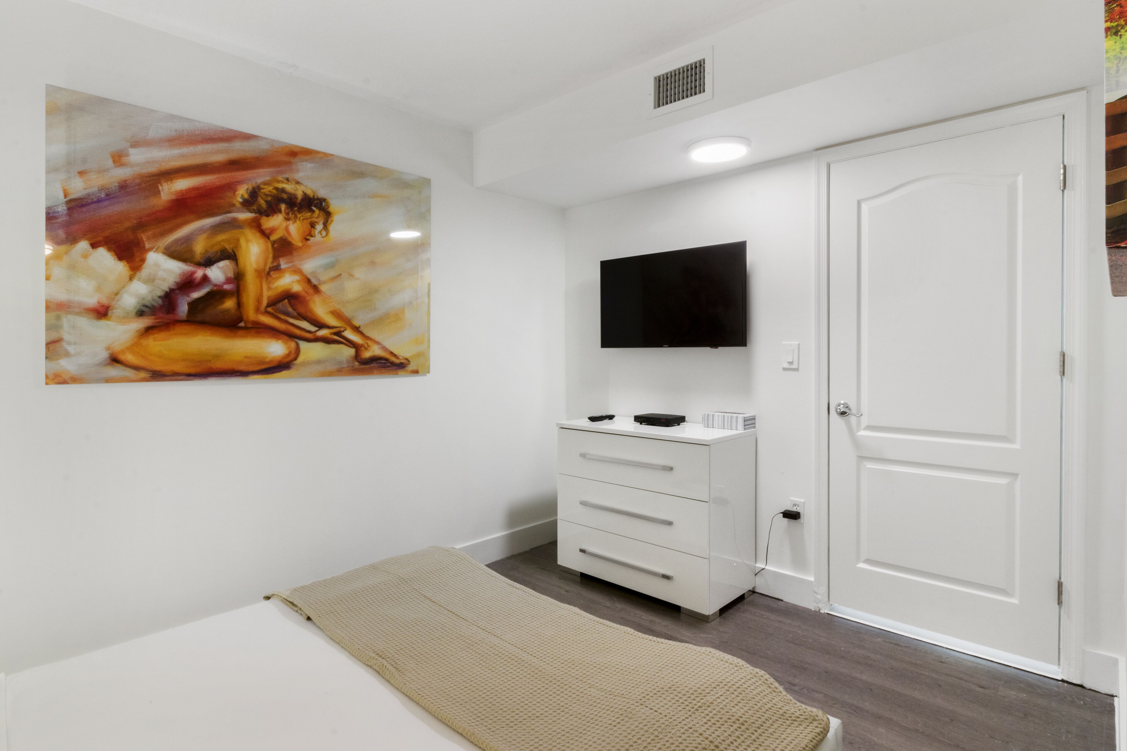 A bedroom with a bed, a dresser, a television, and a painting on the wall.