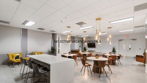 Un espace de restauration moderne et bien éclairé, avec plusieurs tables et chaises, un îlot central et des luminaires suspendus.