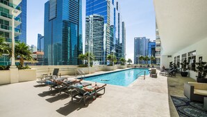 Un espace piscine aménagé sur le toit, avec des chaises longues et une piscine, le tout entouré de grands immeubles.