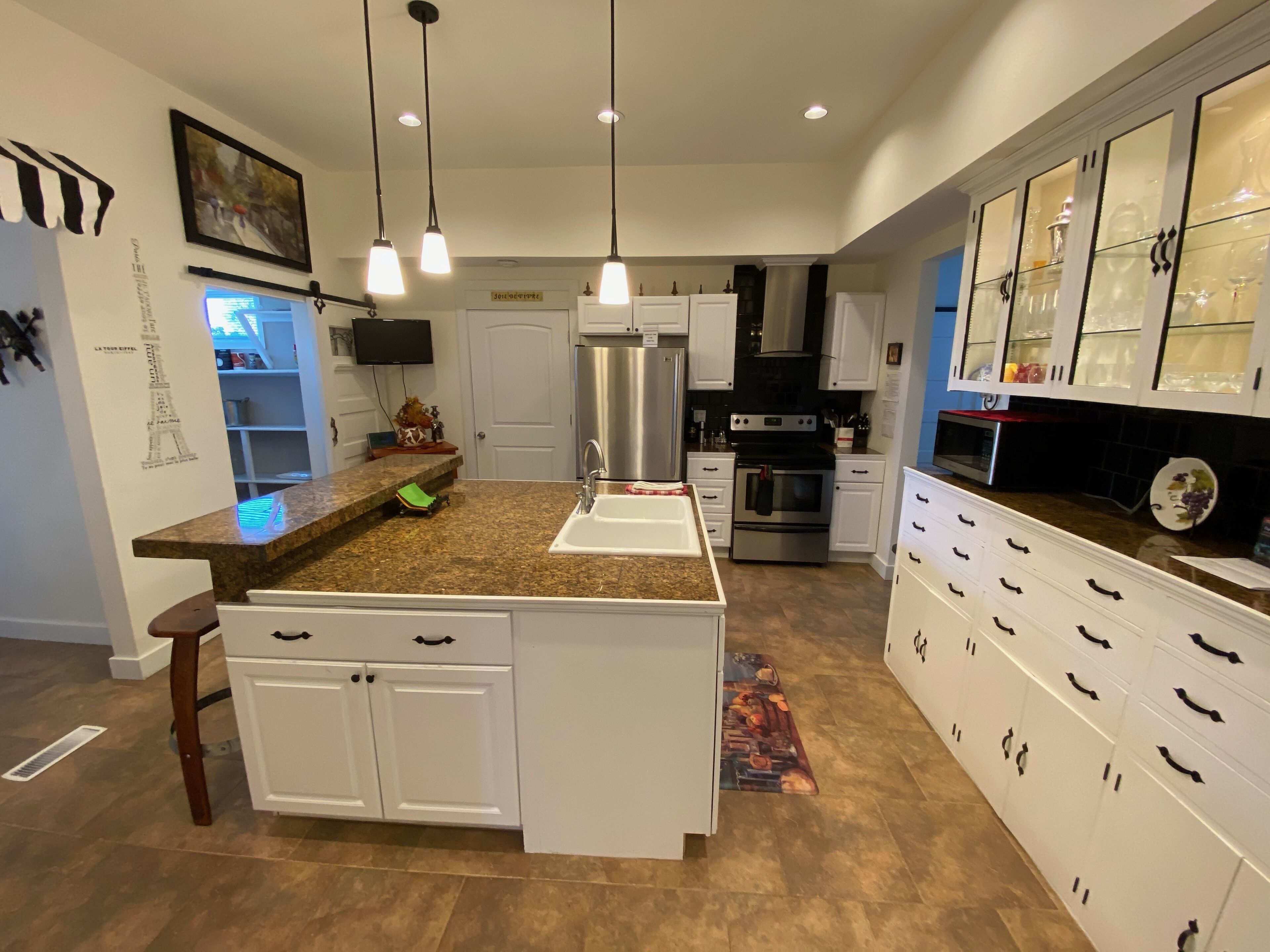 A modern kitchen with granite countertops, white cabinetry, stainless steel appliances, and pendant lighting.