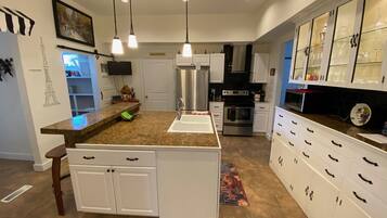 A modern kitchen with granite countertops, white cabinetry, stainless steel appliances, and pendant lighting.