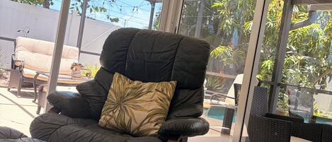 Une chambre moderne dotée d’une grande porte-fenêtre coulissante, d’un fauteuil en cuir noir agrémenté d’un coussin à motifs, d’un pouf assorti et d’une petite table sur laquelle se trouve une tasse.