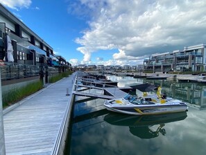 Ein Yachthafen mit vertäuten Booten, einer Holzpromenade und modernen Gebäuden im Hintergrund.
