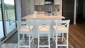 Une cuisine moderne avec des meubles blancs, un îlot central doté de tabourets, un four à micro-ondes et un réfrigérateur.