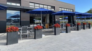 Un espace extérieur aménagé avec des tables et des chaises, des parasols bleus et des jardinières fleuries.