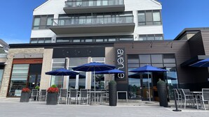 Un bâtiment moderne, avec une enseigne bien visible indiquant « avenue », des places assises en plein air sous des parasols bleus et un ciel dégagé.
