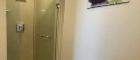 Ducha con mampara de vidrio, panel de control, piso de baldosas e imagen de piedras y flores en la pared.