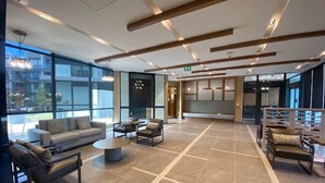 Un hall d’entrée spacieux au design moderne, comprenant un grand espace salon avec des canapés et des fauteuils, une table basse centrale et une grande fenêtre offrant une vue sur l’extérieur.