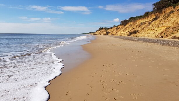 A wide sandy beach with gentle waves, a clear sky, and a rocky cliff on one side. - Sea View House: Large modern Beachfront home with downstairs Bedroom & Bathroom (Lowestoft)