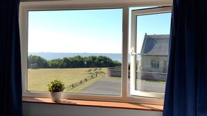 A window with a view of a grassy field, a stone building, and the sea. - Sea View House: Large modern Beachfront home with downstairs Bedroom & Bathroom (Lowestoft)