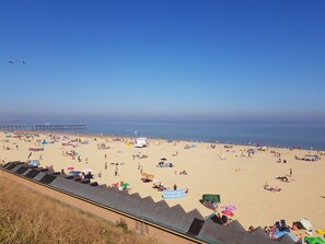 Une plage avec une jetée en arrière-plan, des parasols et des gens qui se détendent.