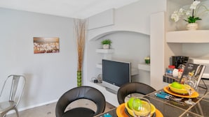 Een moderne eethoek met een zwarte tafel, twee zwarte stoelen, een televisie en een potplant op een witte plank.