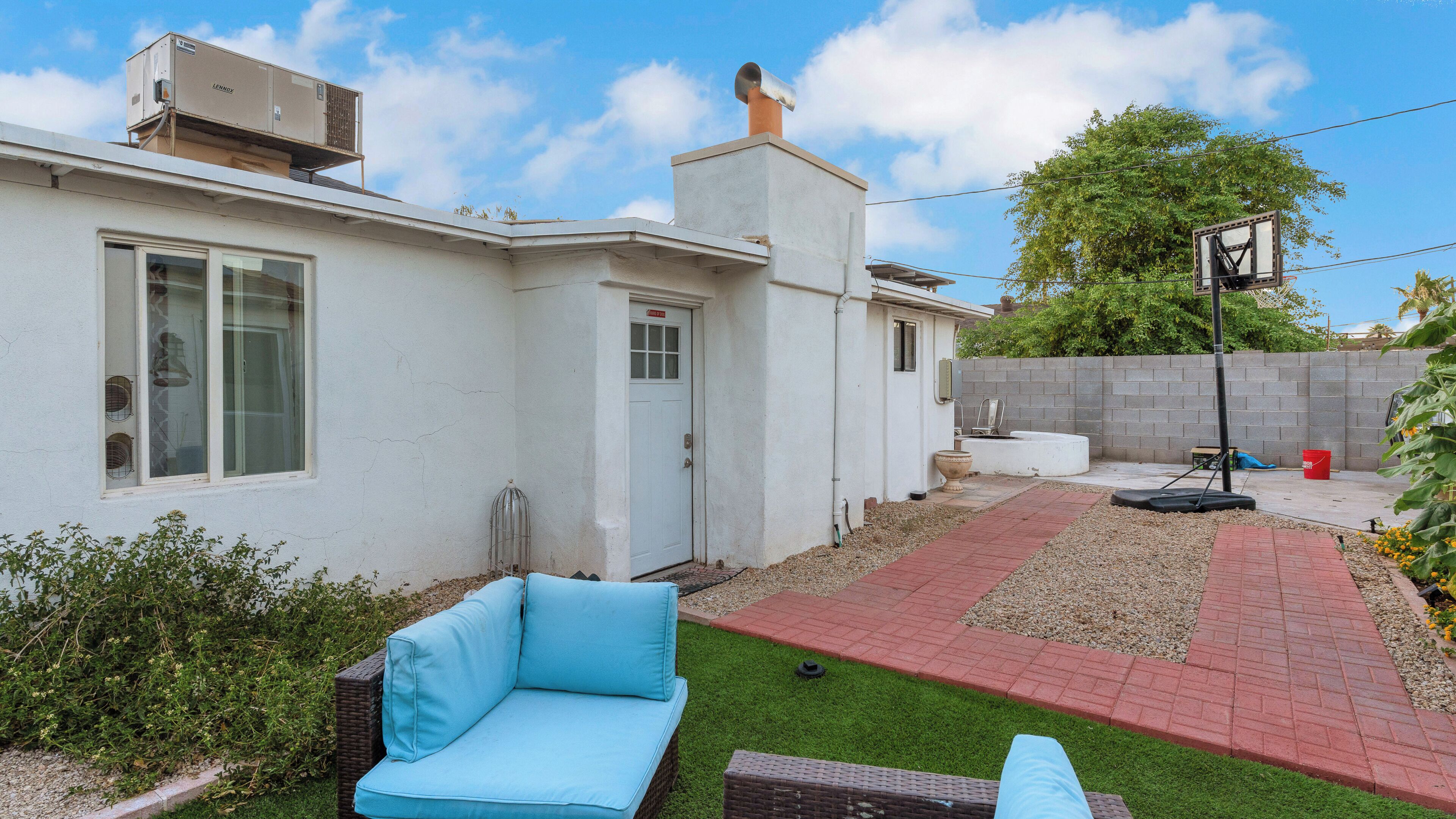 Un jardin à l’arrière d’une maison, avec une maison blanche, un canapé bleu pour l’extérieur, un petit espace aménagé en jardin et un panier de basketball.